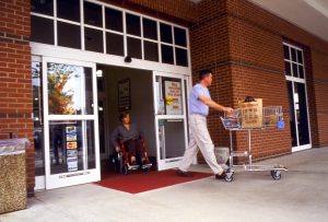 someone is pushing cart out of door and person behind is in wheelchair